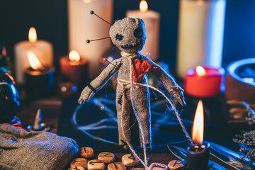 Voodoo doll studded with needles in magical table with candles and occult objects. Magic and dark spooky ritual. Retribution or revenge through witchcraft concept. - obrazy, fototapety, plakaty