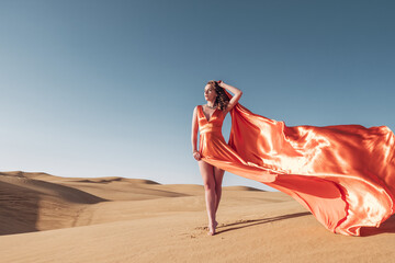 Gorgeous Caucasian woman wearing an orange long dress and posing for the camera in a desert