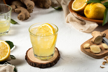 Detox lemon and ginger drink, with ice and a slice of lemon inside the glass, as an immune boosting and weight loss drink on a white textured surface, soft light
