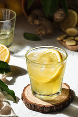 Fresh lemon drink with ginger and a slice of lemon inside the glass, as an immune boosting and weight loss drink, on a white surface, hard light