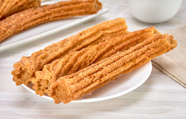 spanish churros covered with sugar and cinnamon on a white plate on a marble surface and white background. close up view.