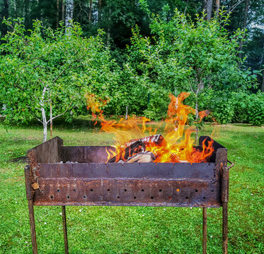a photo of a barbecue in the backyard of a house with a large flame of fire rising from it