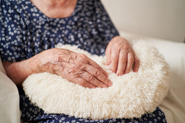 Detail of a 90 year old woman's hands over fluffy pillow