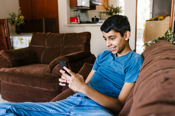 Mexican teen boy having fun with smartphone sitting on sofa at home in Latin America © Marcos