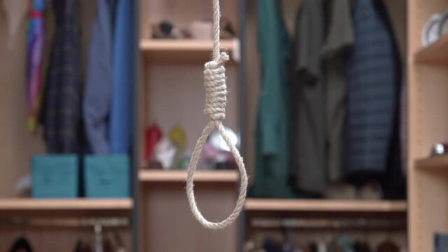 Loop with rope hangs from top to bottom in the apartment, dressing room in blurred background. Punishment of criminals by hanging. The problem of suicide.