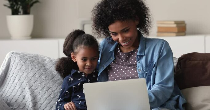 Happy bonding two female generations african ethnicity family using educational computer applications, watching online cartoons, playing game, shopping in internet store, resting on sofa at home.