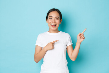 Beautiful happy asian girl in white t-shirt helping with choice, showing way or demonstrating...