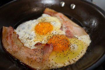 eggs and bacon with black pepper in a cooking pan
