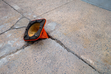 broken weathered sidewalk  with pot hole with orange cone upside-down in hole