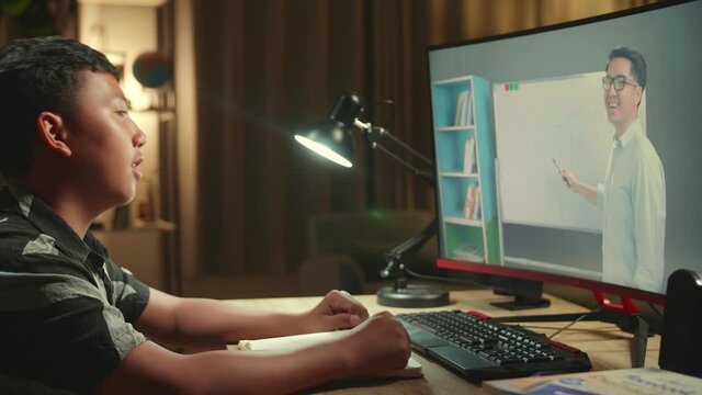 Asian Boy Learning Online From Home, Raising Hand Distance Learning Online At Virtual Lesson Class With Teacher Tutor On Computer Screen By Video Conference
