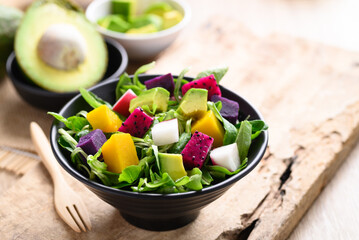 Healthy vegan salad fruits and vegetables with avocado, dragon fruit, radish, pumpkin and corn salad in a bowl on wooden