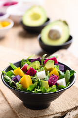 Healthy vegan salad fruits and vegetables with avocado, dragon fruit, radish, pumpkin and corn salad in a bowl on wooden