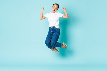 Fashion, beauty and lifestyle concept. Cheerful triumphing, attractive asian girl jumping from...