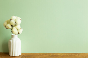 White vase of cotton plant on wooden table. green wall background. Home interior