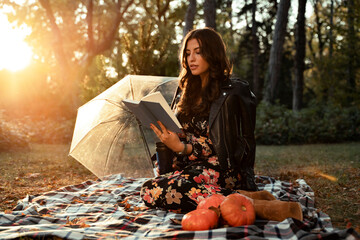 Pretty young adult woman reading a book in fall season in park on blanket 