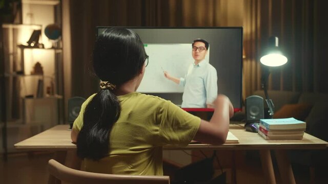 Asian Girl Learning Online From Home, Raising Hand Distance Learning Online At Virtual Lesson Class With Teacher Tutor On Computer Screen By Video Conference
