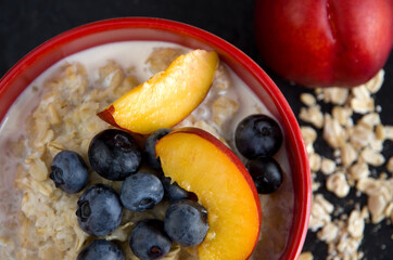 Oatmeal with Blueberries and Nectarines in a Red Bowl with Dark Background