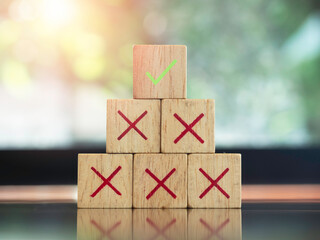 Green check mark icon on top of red cross icons on wooden cube blocks, pyramid steps, on wood table on green nature background. Business success with process management, troubleshooting concept.
