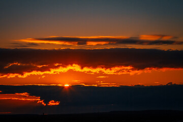 Fototapeta premium the bright sun peeks out from behind the clouds at dawn on a warm summer morning
