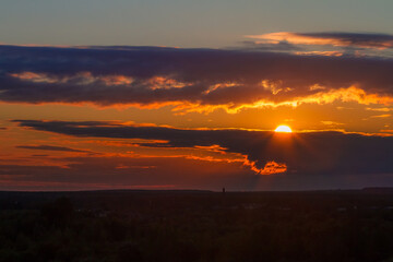 the bright sun peeks out from behind the clouds at dawn on a warm summer morning