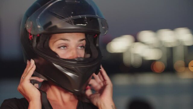 A woman putting on her motorcycle helmet on a background of night city