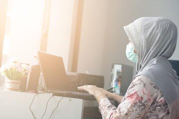 Muslim woman wearing a mask working using a laptop in the office in new normal style. Work at home concept.