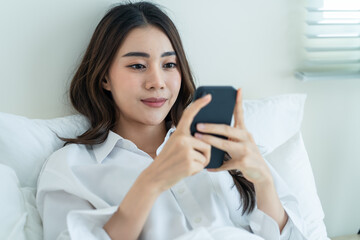Asian attractive woman use mobile phone chat on bed at home in morning.
