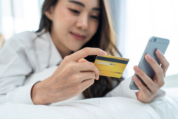 Asian attractive woman enjoy shopping online on bed at home in morning. 