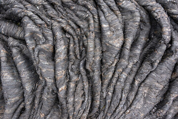 Natural background from solidified volcanic lava. Rope lava is the result of slowing forward flow and accelerating backward flow. Crumpled volcanic stones of Kamchatka Russia
