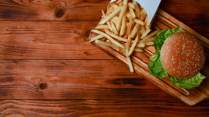 Fish burger and fried potatoes on wooden serving board.