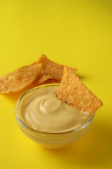 Bowl with cheese sauce and chips on yellow background