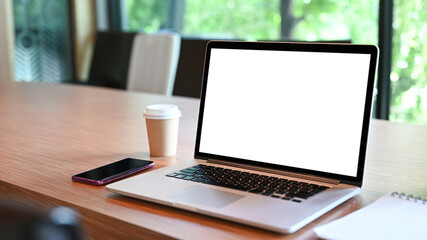 Close up laptop computer with white screen, mobile phone and coffee cup on wooden table.