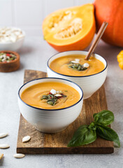 Two bowls of pumpkin cream soup on a wooden board, sprinkled with seeds. Autumn soup.