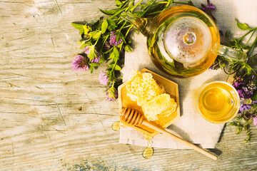 Tea with fresh leaves of summer herbs clover natural liquid honeycomb in glass teapot cup on a rustic wooden background