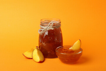 Jar and bowl of peach jam and ingredients on orange background