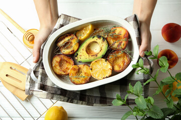Female hands hold baking dish with grilled peach, top view