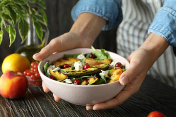 Woman in apron holds plate with salad with grilled peach