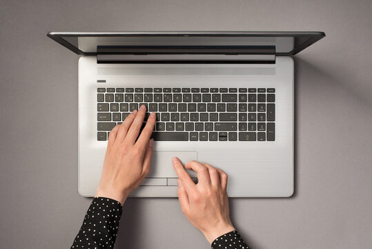 First person top view photo of hands using laptop touchpad and typing on keyboard on isolated grey background