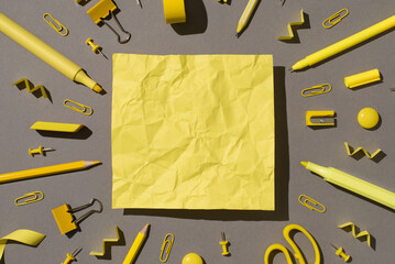 Top view photo of yellow crumpled sheet surrounded by yellow stationery school supplies felt pens pencils pins binder clips magnets scissors sharpeners eraser isolated grey background with blank space