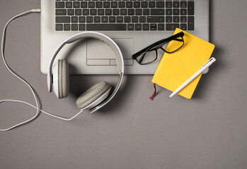 Top view photo of laptop keyboard wired white headphones glasses pen and yellow reminder on isolated grey background