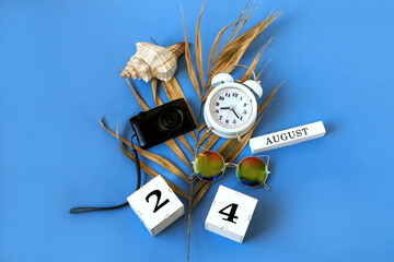Calendar for August 24 : the name of the month of August in English, cubes with the number 24, a dry palm leaf, a shell, a camera, a watch, sunglasses on a blue background, a top view