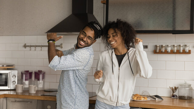 Happy African hipster couple dancing together in modern kitchen. Young active boyfriend and girlfriend listen music moving at home enjoy carefree day off weekend spend romantic date in cozy apartment