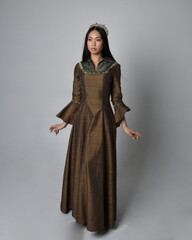 Naklejka premium Full length portrait of beautiful young asian woman with long hair wearing medieval fantasy gown and golden crown. Graceful standing pose, isolated on studio background.