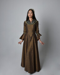 Full length  portrait of beautiful young asian woman with long hair wearing medieval fantasy gown and golden crown. Graceful standing pose,  isolated on studio background.