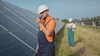 An employee of a power plant transmits commands by walkie-talkie. Happy caucasian adult engineer in...