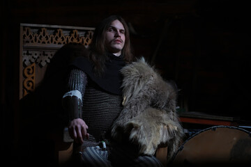 A mighty hero with long hair in chain mail armor in an ancient hall. Medieval warrior in the knight's chambers.