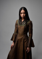 Naklejka premium Close up portrait of beautiful young asian woman with long hair wearing medieval fantasy gown. Graceful pose with gestural hands, isolated on studio background.