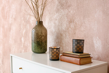 Candles with vase and books on shelf near color wall