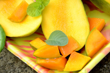 Fototapeta na wymiar closeup the sliced ripe green yellow mango fruit with green mint leaves and chilly in the tray over out of focus grey brown background.