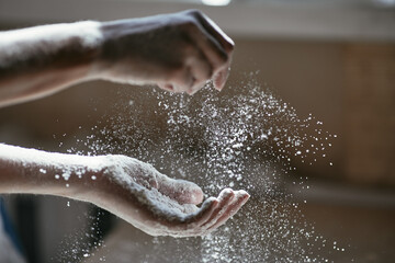 Fototapeta premium Girl scattering flour in the air, close-up photo of hands